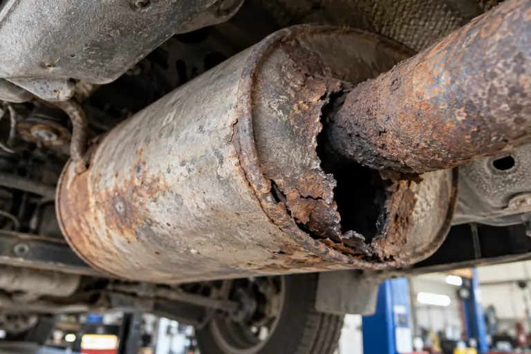 Exhaust Leak & Muffler Repair Cost Guide — Signs You Need a Fix 3 Close-up of a corroded muffler with a visible hole